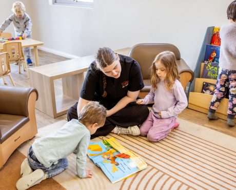 Early learning educator reading a book with young children in a childcare room.